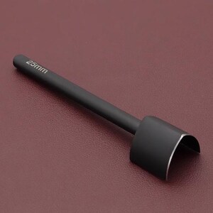 May include: A black leathercraft tool with a curved cutting edge. The tool has a long, cylindrical handle with the measurement "25mm" printed on it. The tool is designed for cutting leather and other materials. The tool is shown against a maroon background.