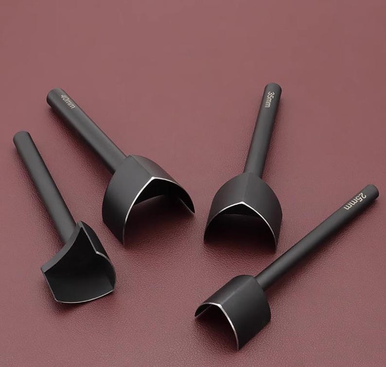 May include: Four black leathercraft tools with curved cutting edges and long handles. The tools are labeled with sizes: 25mm, 35mm, and 40mm. The tools are arranged on a burgundy surface.
