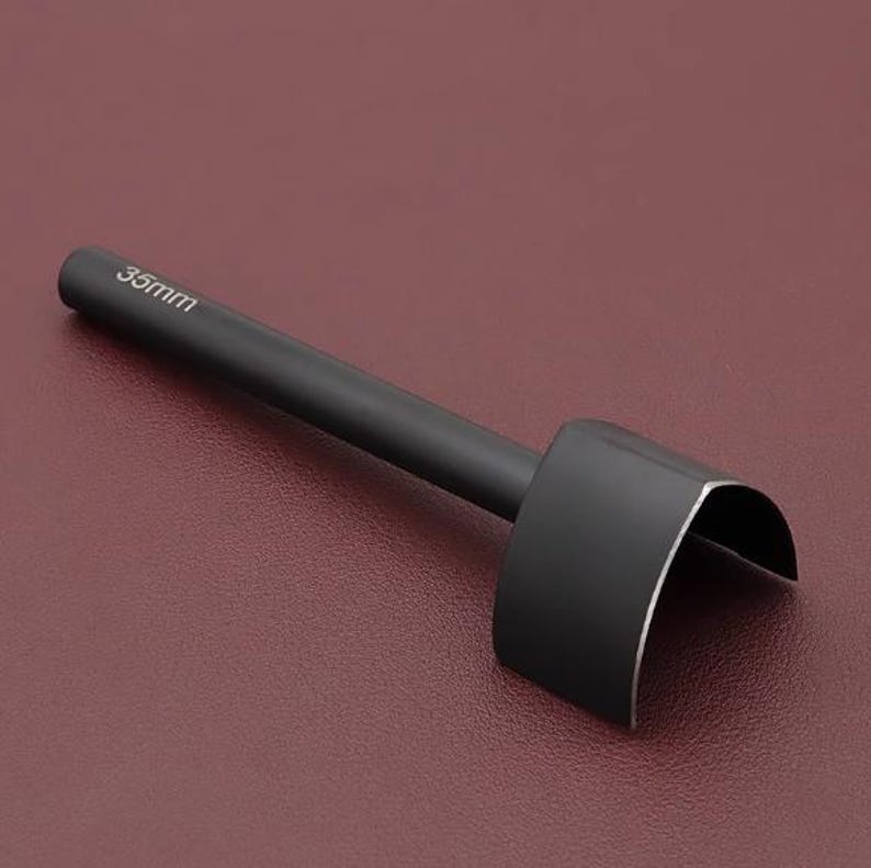 May include: A black leathercraft tool with a curved cutting edge. The tool has a cylindrical handle and a blade that is 35mm wide. The tool is designed for cutting leather and other materials.