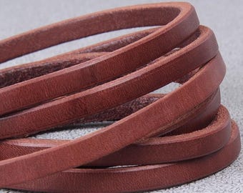 May include: Close-up of several strands of brown leather cord, tightly coiled. The leather has a slightly textured surface and a rich, warm color. The cords are arranged in a layered, overlapping pattern.