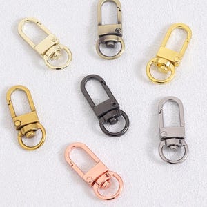 May include: An assortment of metal swivel clasps in various colors, including gold, bronze, silver, and rose gold. These clasps feature a spring-loaded mechanism and a circular ring for attaching to bags or other accessories.