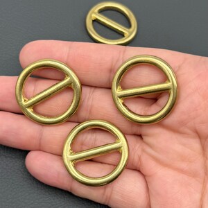 May include: A collection of four brass-colored metal rings with a bar across the center. The rings are circular with a smooth, polished finish. The objects are likely hardware components for leathercraft or similar projects.