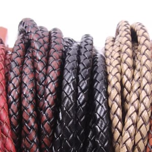 May include: Close-up of several braided leather cords in various colours, including red, black, and tan. The cords are tightly woven, showcasing a textured surface. The image highlights the different shades and the craftsmanship of the leather.