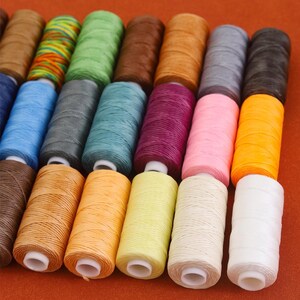 May include: A collection of colorful spools of thread in various shades, including brown, green, blue, gray, pink, and orange. The spools are neatly arranged, showcasing the diverse color palette. Ideal for crafting and sewing projects.