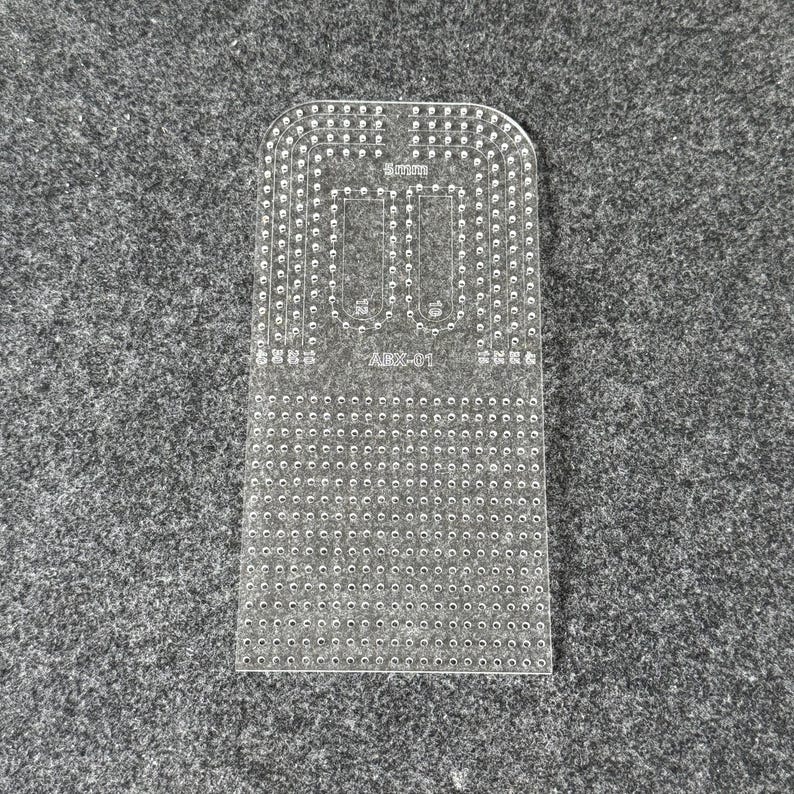Peut inclure: Un gabarit de maroquinerie en acrylique transparent avec un bord sup&eacute;rieur arrondi, de nombreux trous perc&eacute;s avec pr&eacute;cision et des marquages grav&eacute;s incluant 5mm, 10, 15, 20, 25, 30, ainsi que le texte ABX-01 pour la couture du cuir.