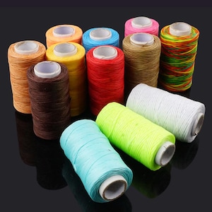 May include: A collection of colorful spools of waxed thread, including shades of brown, red, yellow, blue, green, pink, and white. The spools are cylindrical with a central cardboard core. The threads are tightly wound, creating a textured appearance.
