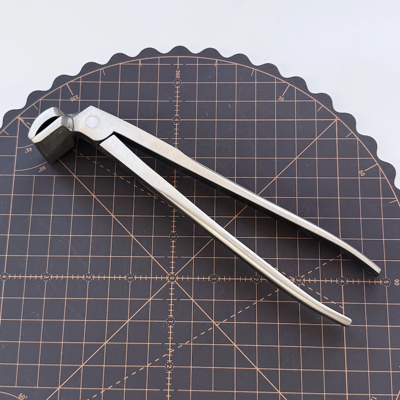 Puede incluir: Una tenaza de herrador de metal plateado, dise&ntilde;ada para recortar cascos de caballos. La herramienta tiene un cabezal de corte y mangos largos para hacer palanca. Se encuentra sobre una esterilla de corte negra.