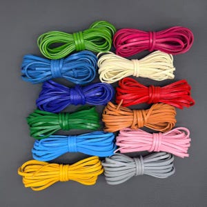 May include: A collection of twelve coiled leather cords in various colors including green, blue, red, yellow, pink, orange, gray, and cream. Each cord is neatly wound into a circular bundle, displaying a smooth, flat texture and consistent width.