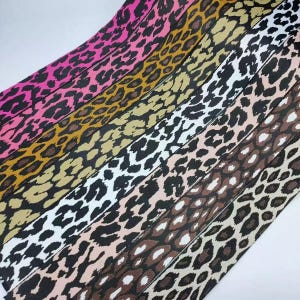 May include: A collection of six parallel fabric strips featuring various leopard print patterns in distinct color combinations including hot pink, mustard yellow, black and white, beige and black, and brown and tan with dark spots.