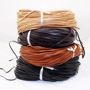 Puede incluir: Una pila de cuatro paquetes de tiras de cuero en varios colores: beige, marrón oscuro, marrón medio y negro. Cada paquete está atado con hilo blanco. Las tiras de cuero son finas y planas.