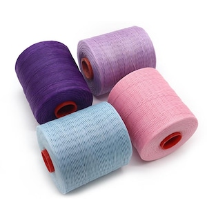 May include: Four spools of colorful thread in shades of purple, lavender, pink, and light blue. Each spool has a red core. The threads are tightly wound, suggesting they are for crafting or sewing projects.