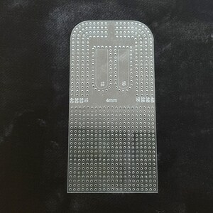 Peut inclure: Un gabarit en acrylique transparent pour le travail du cuir, dot&eacute; d'un sommet arrondi et d'une base rectangulaire. L'outil est perfor&eacute; de nombreux petits trous dispos&eacute;s en rang&eacute;es et colonnes, avec les chiffres 10, 12, 15, 20, 25, 35, 40, 45 et 4mm.