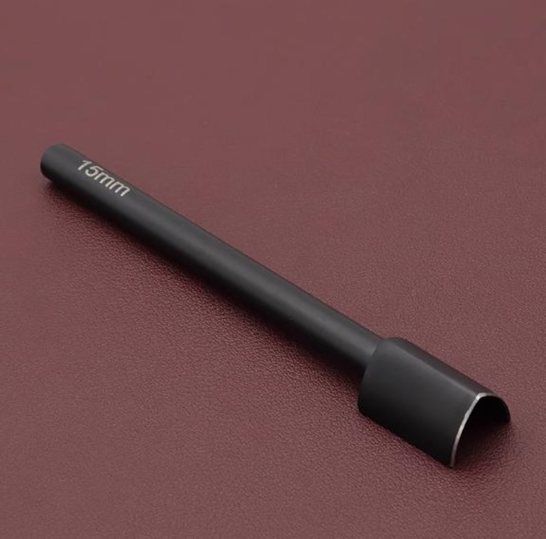 May include: A black leathercraft tool with a cylindrical handle and a curved cutting edge. The text "15mm" is printed on the handle. The tool is designed for cutting leather and similar materials.