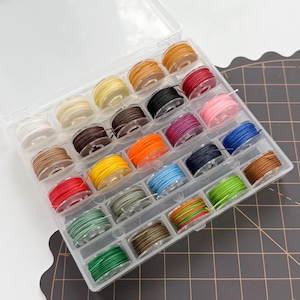 May include: A clear plastic organizer filled with spools of colorful thread. The thread colors include white, yellow, brown, red, pink, blue, green, and orange. The spools are neatly arranged in individual compartments, ideal for sewing and crafting projects.