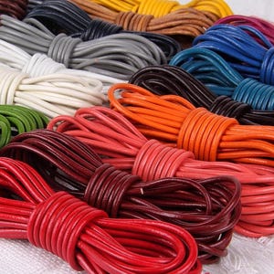 Könnte beinhalten: Eine Sammlung farbiger Lederkordeln in verschiedenen Farbtönen, darunter Rot, Orange, Braun, Blau und Grün. Die Kordeln sind eng gewickelt und zeigen ihre glatte Textur und lebendigen Farben. Ideal für Bastelarbeiten und Schmuckherstellung.