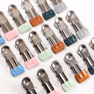 May include: A selection of stainless steel clothes pegs with coloured rubber ends. The pegs feature a variety of colours, including blue, pink, green, orange, and grey. These clothes pegs are designed for hanging laundry.