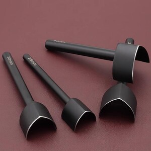 May include: A set of three black leathercraft tools with silver edges. The tools have different sizes, with measurements of 25mm, 30mm, and 40mm. The tools are arranged on a burgundy surface.