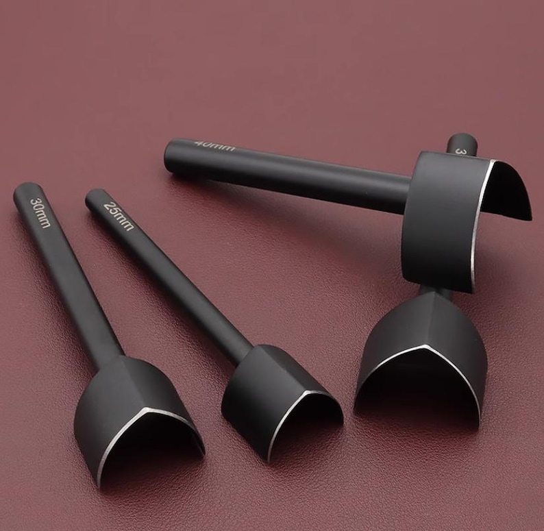 May include: A set of three black leathercraft tools with silver edges. The tools have different sizes, with measurements of 25mm, 30mm, and 40mm. The tools are arranged on a burgundy surface.