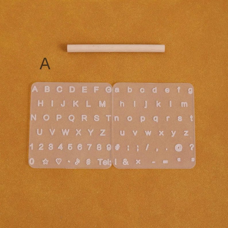 May include: A clear plastic alphabet and number stencil set with uppercase and lowercase letters, numbers, and symbols. Includes a small wooden dowel. The text "Tel: ! & x" is visible.