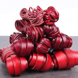 Può includere: Un insieme di strisce di pelle rosso scuro, arrotolate e disposte in una composizione a strati. La pelle ha una finitura liscia e un colore intenso. La disposizione suggerisce un tema decorativo o artigianale.