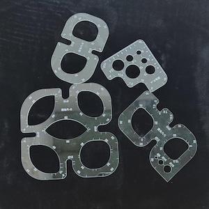 Puede incluir: Cuatro plantillas transparentes de acrílico con diversas formas, bordes curvos, agujeros y marcas de medición en centímetros. Estas herramientas están diseñadas para trabajos de artesanía o diseño, con etiquetas de texto.