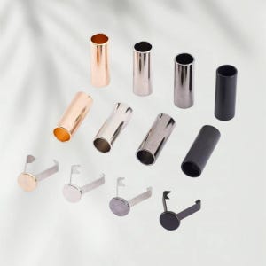 May include: A collection of four cylindrical metal cord ends and four matching metal pronged fasteners in rose gold, silver, gunmetal, and matte black finishes. Each cylindrical piece features a hollow center, while the fasteners have flat circular tops.