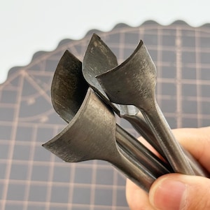 May include: Close-up of several metal leather working tools. The tools have a curved blade design and are held together. The tools are a dark grey colour and appear to be made of steel. The background is a grey cutting mat.