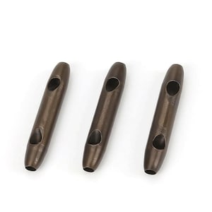 Pode incluir: Três ilhós de metal de cor bronze, cada um com dois orifícios ovais. Os ilhós são cilíndricos com extremidades arredondadas e estão dispostos sobre um fundo branco. Estes são provavelmente usados para artesanato ou trabalhos em couro.