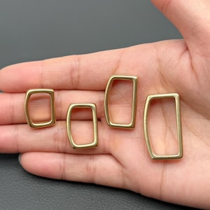 Könnte beinhalten: Vier rechteckige Ringe in Messingfarbe mit abgerundeten Ecken. Die Ringe werden vor einem neutralen Hintergrund gezeigt. Diese Metallringe werden wahrscheinlich für Bastelarbeiten oder die Schmuckherstellung verwendet.