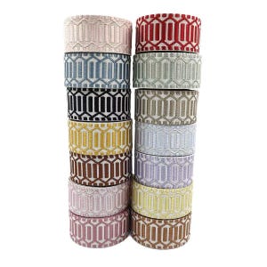 Peut inclure: Deux piles verticales de rouleaux de ruban tissé présentant un motif géométrique répétitif de barres verticales et de lignes interconnectées. Les rubans sont disponibles en plusieurs couleurs, dont le rouge, le bleu, le noir, le jaune, le marron, le rose, le vert et le beige.