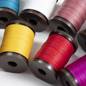 May include: A collection of colorful spools of thread. The spools are in various colors, including blue, white, pink, yellow, red, and purple. Each spool is wound with thread and has a brown base.