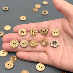 May include: A collection of various wooden buttons in different sizes and designs. Some buttons have two or four holes, while others feature etched patterns like flowers, grids, and baseball stitching. The buttons are light brown in color.