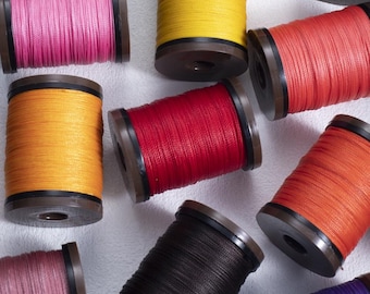 May include: A collection of colorful spools of thread, including shades of pink, yellow, red, orange, black, and purple. The thread is tightly wound on brown spools with black accents, ideal for sewing and crafting projects.