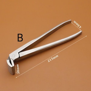 Puede incluir: Un cascanueces de acero inoxidable con un dise&ntilde;o articulado. La herramienta mide 21,5 cm de largo, 4,3 cm de ancho y 3,8 cm de alto. La letra "B" est&aacute; impresa en el lateral.