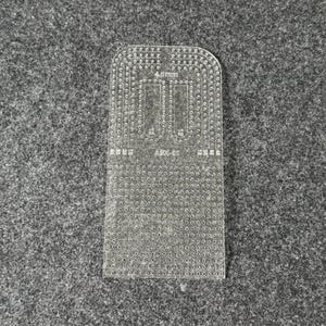 Peut inclure: Un gabarit de maroquinerie en acrylique transparent avec un bord sup&eacute;rieur arrondi et une grille de trous de couture d&eacute;coup&eacute;s avec pr&eacute;cision. L'outil porte l'inscription 4.5mm et ABX-01, ainsi que des indicateurs num&eacute;riques de guidage.