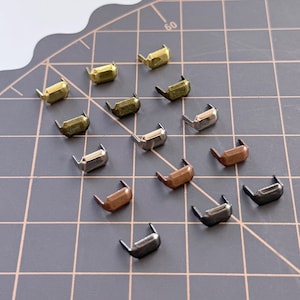 May include: A collection of metal rivets in various finishes, including gold, silver, and bronze. The rivets are arranged on a gray cutting mat, showcasing their shape and color variations. These decorative rivets are ideal for leathercraft and adding embellishments.