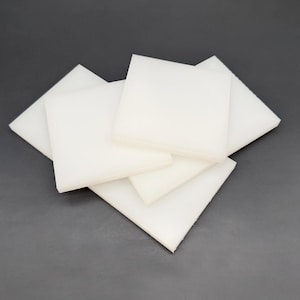 May include: A collection of white, square-shaped foam pads are stacked and slightly overlapping against a gray background. The pads appear to be of varying sizes, with a smooth, clean surface. The lighting highlights the edges, creating subtle shadows.