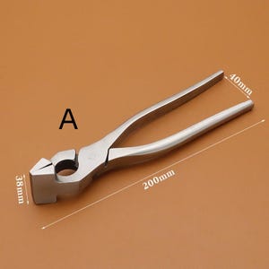 Puede incluir: Una herramienta de herrero de metal plateado, con cabeza de martillo y mangos tipo alicates. La herramienta mide 20 cm de largo, con una cabeza de 3,8 cm de ancho y 4 cm de alto. La letra "A" es visible.
