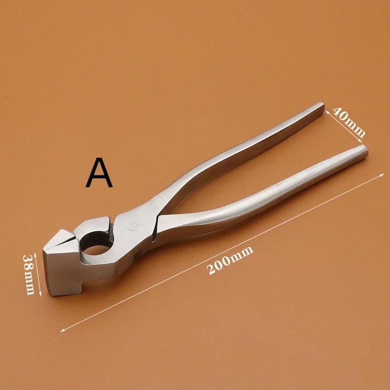 Puede incluir: Una herramienta de herrero de metal plateado, con cabeza de martillo y mangos tipo alicates. La herramienta mide 20 cm de largo, con una cabeza de 3,8 cm de ancho y 4 cm de alto. La letra "A" es visible.