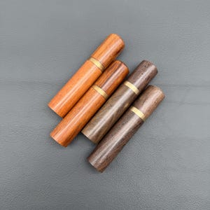 Puede incluir: Cuatro palilleros de madera en tonos marrones, dispuestos en diagonal. Cada soporte tiene una banda de latón en el centro. Las vetas de la madera varían de claras a oscuras, creando una estética natural y rústica.