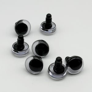 May include: A collection of seven plastic toy eyes with black pupils and clear, rounded outer shells. Each eye has a black, threaded post for attachment. The eyes are designed for crafts and toy making.