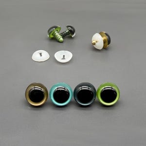May include: A collection of doll eyes in various colors and styles. The assortment includes green, blue, black, and gold-colored eyes, along with clear plastic backing pieces and screw-in eye components.