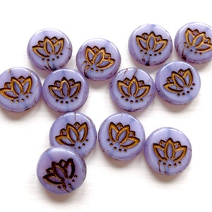 May include: A collection of 12 purple glass beads with gold lotus flower designs. The beads are round and have a slightly textured surface.
