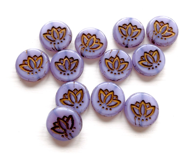 May include: A collection of 12 purple glass beads with gold lotus flower designs. The beads are round and have a slightly textured surface.