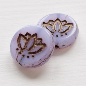 May include: Two round, lavender glass beads with a gold lotus flower design. The beads have a slightly distressed look.