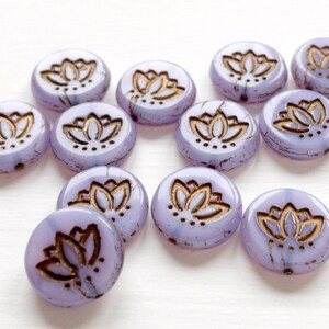 May include: A group of 12 round, lavender glass beads with a gold lotus flower design. The beads have a crackled finish.