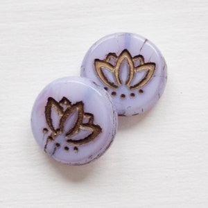 May include: Two round, purple glass buttons with a gold lotus flower design. The buttons have a mottled, textured surface.