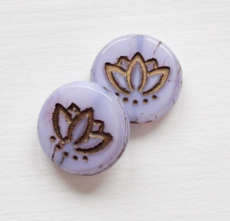 May include: Two round, purple glass buttons with a gold lotus flower design. The buttons have a mottled, textured surface.