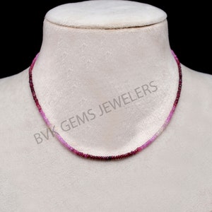 May include: A pink and red gemstone necklace with a gradient of color. The necklace is made of small, round beads and is strung on a thin chain. The necklace is displayed on a white mannequin.