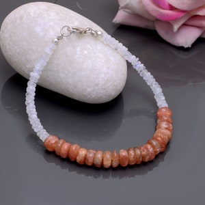 May include: A silver bracelet with white moonstone beads and orange sunstone beads. The bracelet is made with a silver clasp.